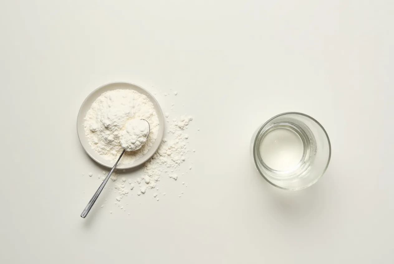 An overhead flat-lay of collagen powder, a glass of water, and a small scoop on a neutral surface